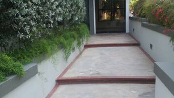 A concrete pathway leading to a building entrance, flanked by low walls and greenery.