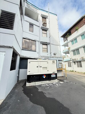 Un véhicule utilitaire est garé devant un immeuble à plusieurs étages, dont la façade est blanche et qui possède de nombreuses fenêtres.