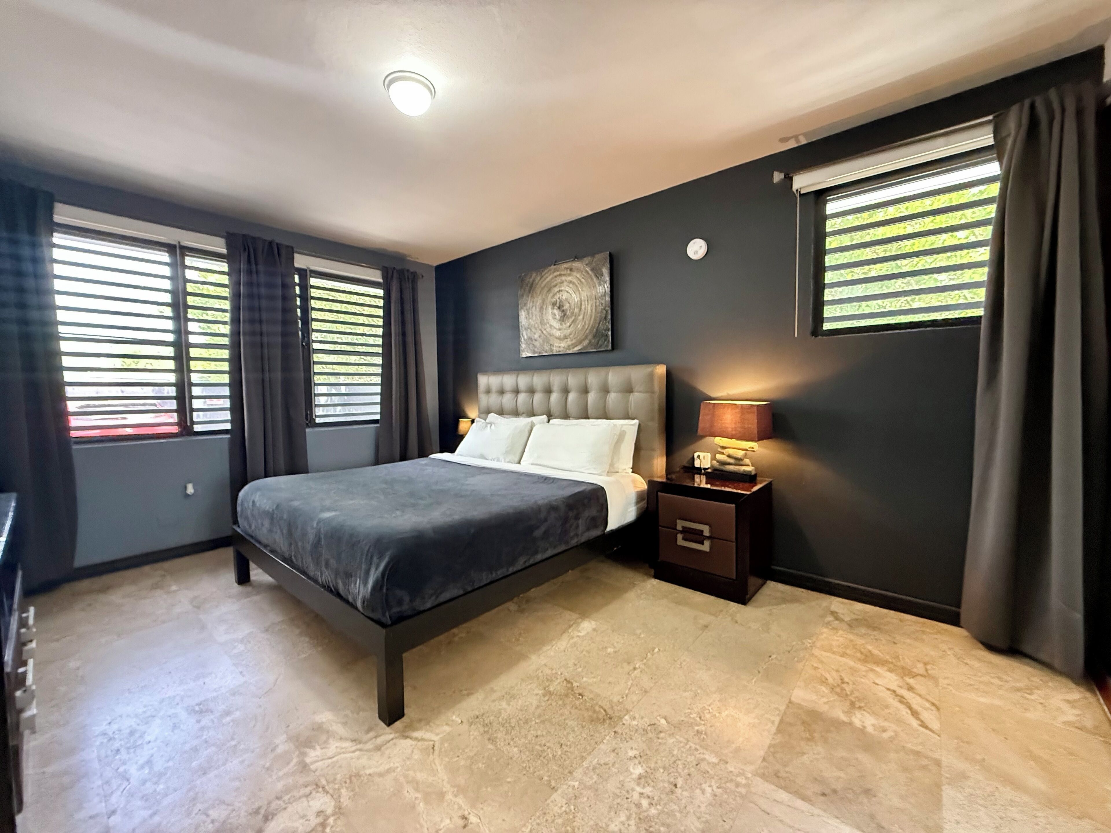 A bedroom with a large bed, a nightstand with a lamp, and a wall clock.