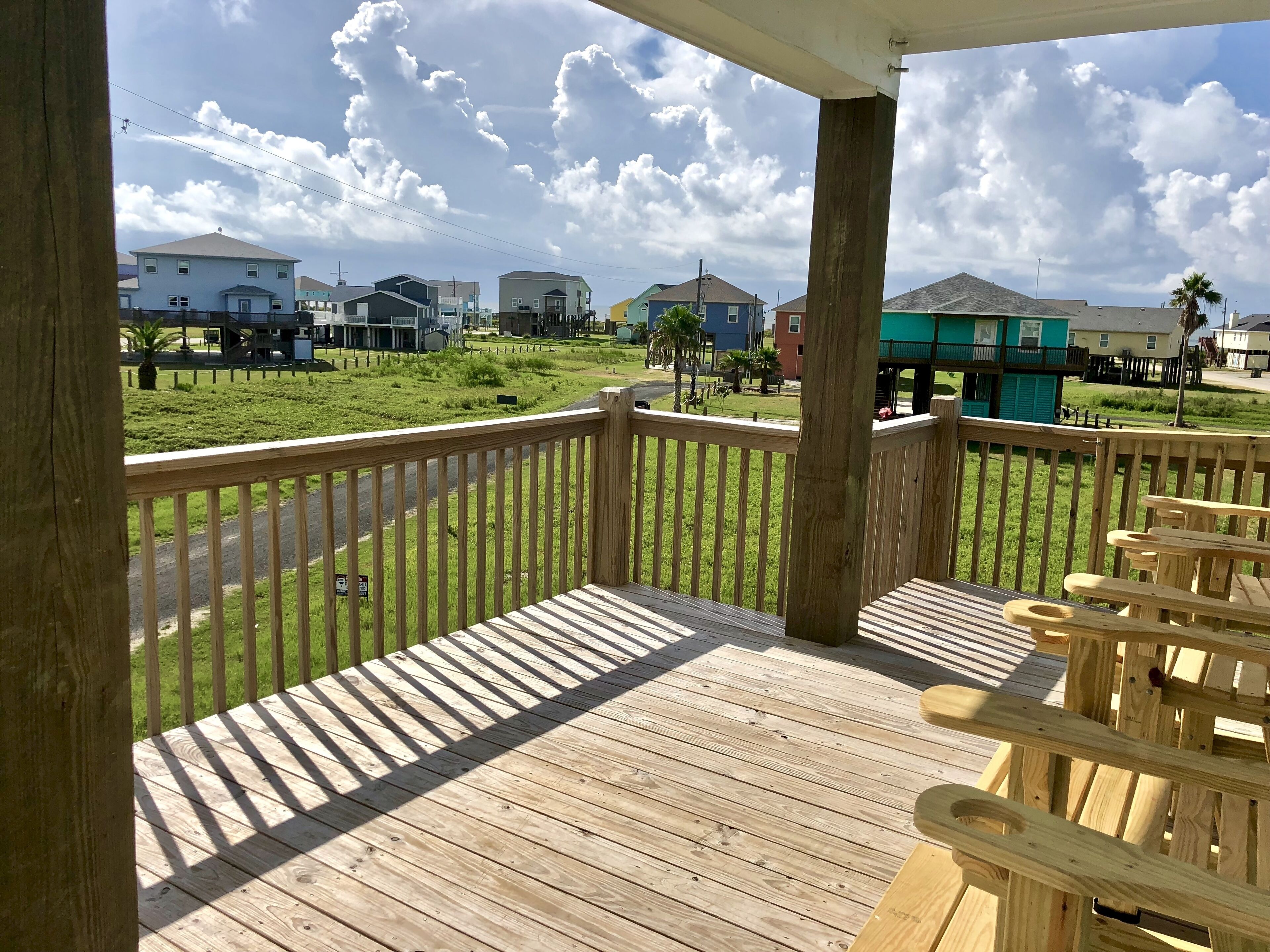 A wooden deck with a view of a residential area, including houses and a grassy field.