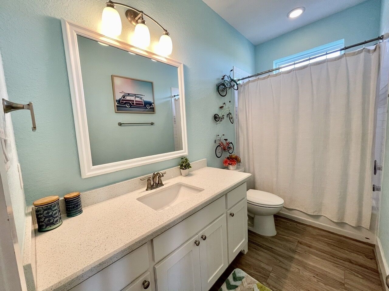 A bathroom with a white vanity, a large mirror, a toilet, and a shower curtain.