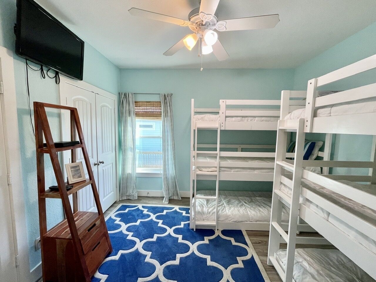 A room with bunk beds, a ceiling fan, a TV, and a wooden ladder.