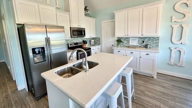 A kitchen with white cabinetry, a stainless steel refrigerator, a microwave, and a sink with stools.