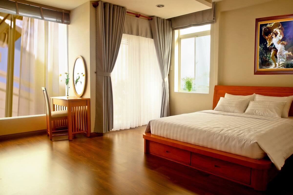 Ein Schlafzimmer mit einem Holzbett, einem Schreibtisch mit Stuhl und einem Fenster mit Vorhängen.