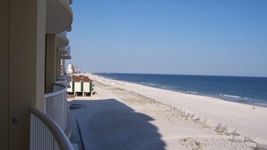 Ein Balkon mit Blick auf einen Strand und klare Sicht auf das Meer, mit einigen Gebäuden in der Ferne.