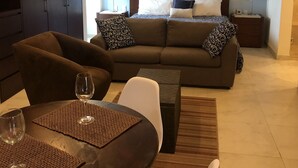 Ein modernes Hotelzimmer mit Schlafsofa, Essbereich mit Tisch und Stühlen, Deckenventilator und einer Wanddekoration.