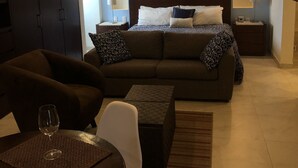 Ein modernes Hotelzimmer mit einem Bett, einer Couch, einem Esstisch mit einem Weinglas und einem Deckenventilator.