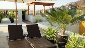 Eine Dachterrasse mit zwei Liegestühlen, einer Pergola und Kübelpflanzen.