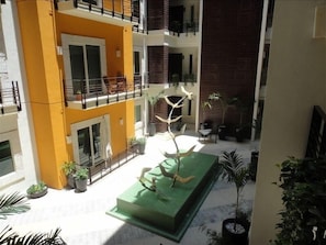 Stunning multi-level building with balconies, potted plants, and a sculptural tree element in the courtyard.