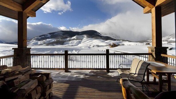 Una terraza de madera con vistas a montañas nevadas y un cielo despejado.