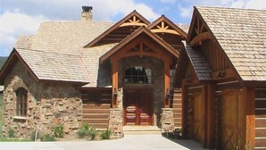 Una cabaña de troncos con cimientos de piedra, una entrada central con puerta de madera y una chimenea.