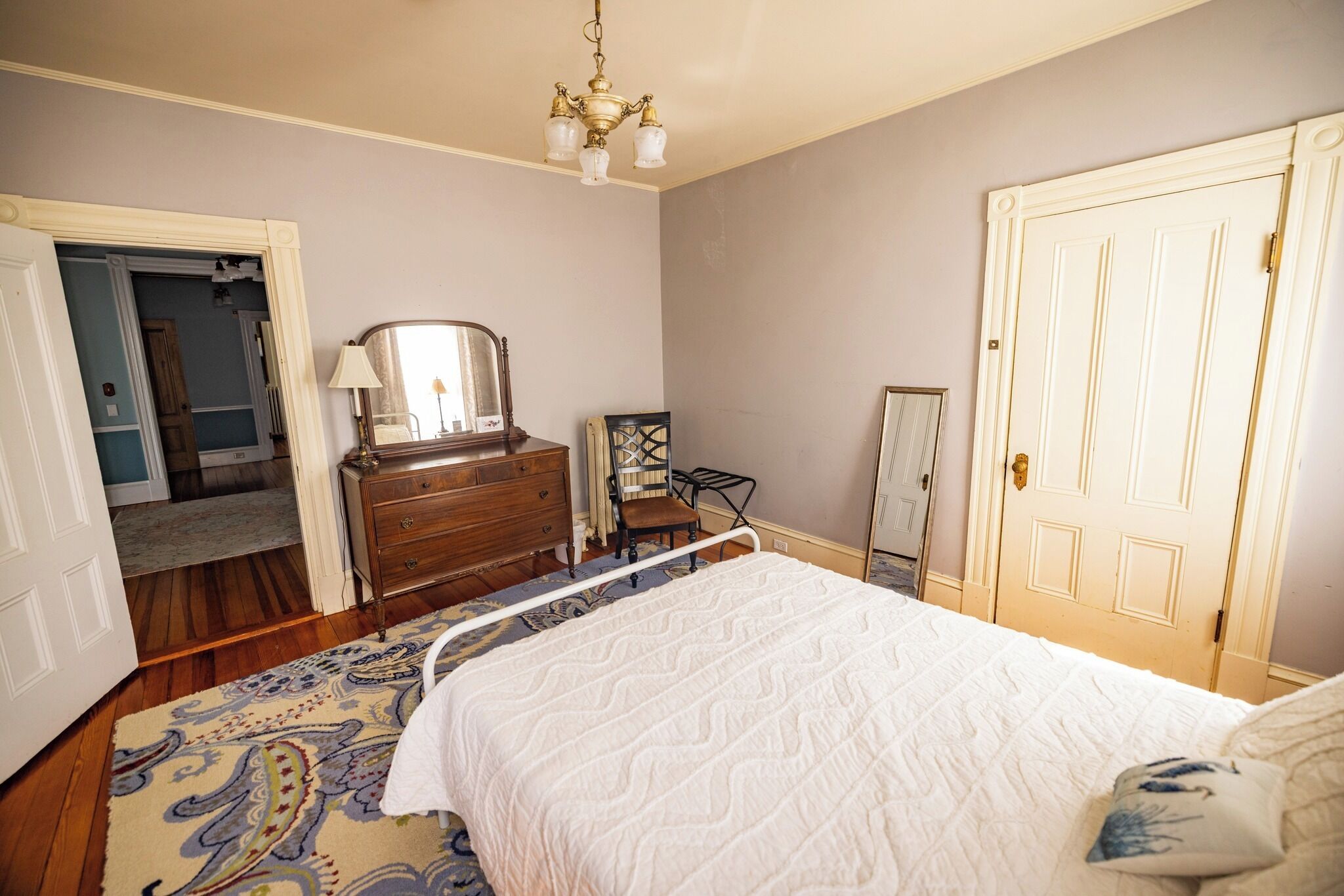 Ein Schlafzimmer mit Bett, Kommode, Spiegel und einer Tür.