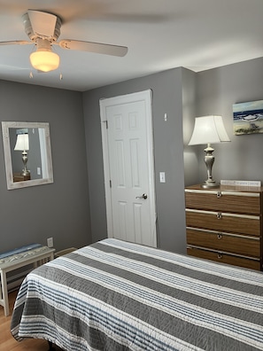 A bedroom with a bed, a dresser, a mirror, a ceiling fan, and a painting on the wall.