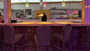 Un restaurant amb zona de bar, caires de vimet i una cuina al fons.