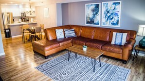A living room with a brown leather sectional sofa, a wooden coffee table, and patterned rugs.