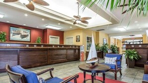 A lobby with wooden furniture, a sailboat model, ceiling fans, and a reception desk. - Harbour Lights™ - 1 Bedroom Deluxe (Myrtle Beach)