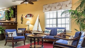 A living room with a red rug, blue sofas, wooden chairs, a small sailboat model, and a ceiling fan. - Harbour Lights™ - 1 Bedroom Deluxe (Myrtle Beach)