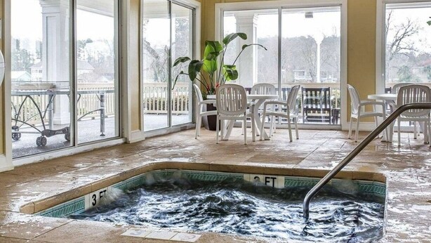 A heated indoor pool with a view of the outside, surrounded by white chairs and a potted plant. - Harbour Lights™ - 1 Bedroom Deluxe (Myrtle Beach)