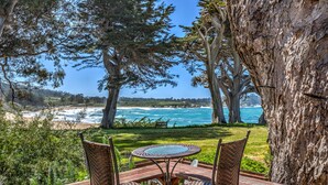 Terraza de madera con sillas de mimbre y una mesa redonda con vista a la playa y al océano.