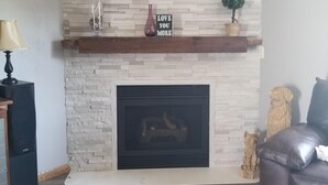 A living room with a fireplace, a wooden mantel, and a stone wall. - 2 bed/2 bath Townhouse on a Quiet cul de sac with backyard views and a Hot tub (Sheboygan)