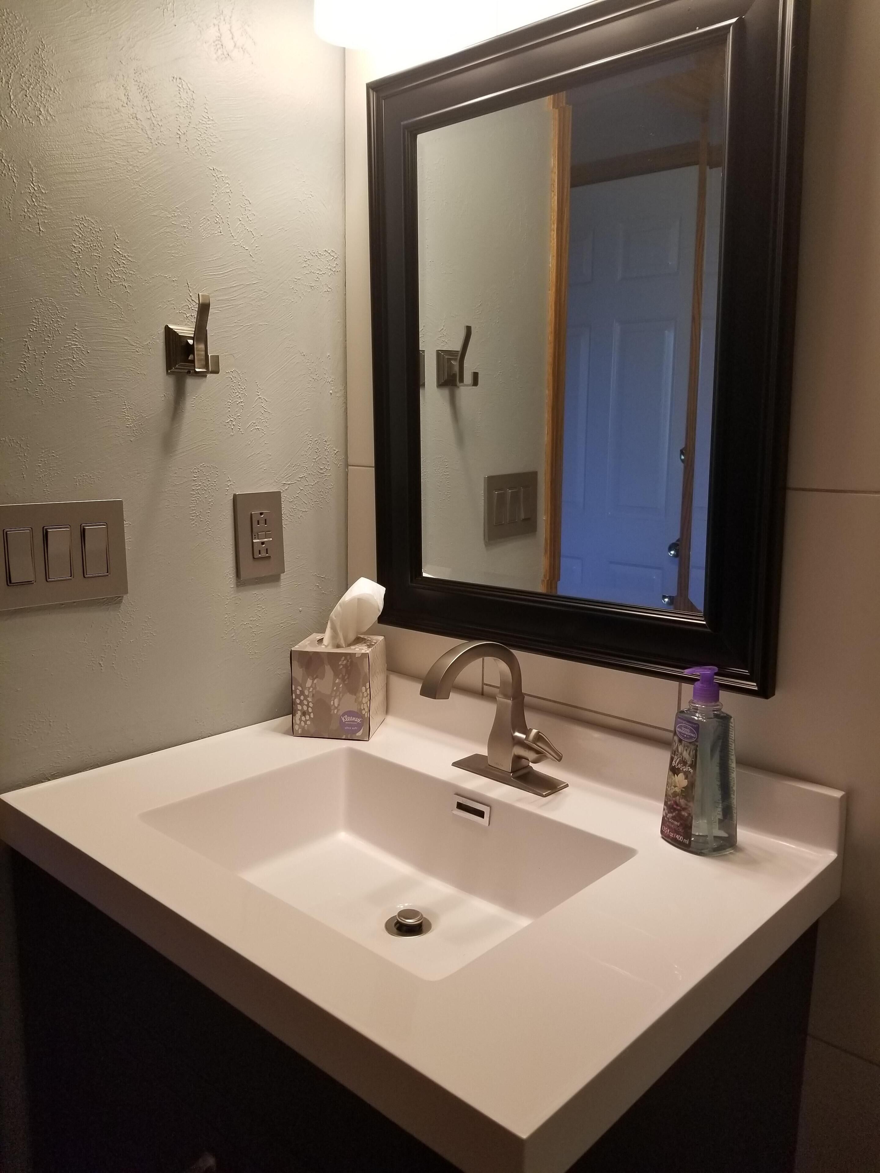 Une salle de bain avec un lavabo blanc, un miroir, une boîte de mouchoirs et un distributeur de savon.
