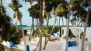 A beach setting with white canopies and hammocks, a thatched structure, and a view of the ocean. - Cancun Grand Mayan Master Room, 2 Adults, 2 children (Playa del carmen)