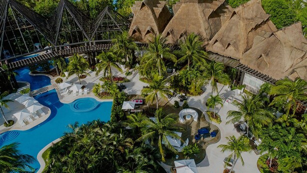 An aerial view of a resort with a large pool, palm trees, and thatched-roof structures. - Cancun Grand Mayan Master Room, 2 Adults, 2 children (Playa del carmen)
