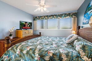 Quarto com uma cama, televisão, cômoda e janela com cortinas.