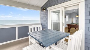 Un balcón techado con vistas al océano, una mesa de billar y una puerta que da a una piscina.