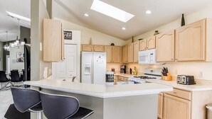 A modern kitchen with a central island, bar stools, a refrigerator, microwave, stove, and wooden cabinets.