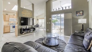 A modern living room with a Star Wars sign, a flat-screen TV, a leather sofa, and a glass coffee table.