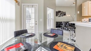 A modern dining area with a glass table, black chairs, and a kitchen area in the background.