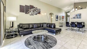 A modern living room with a sectional sofa, a glass coffee table, and a dining area with a table and chairs.