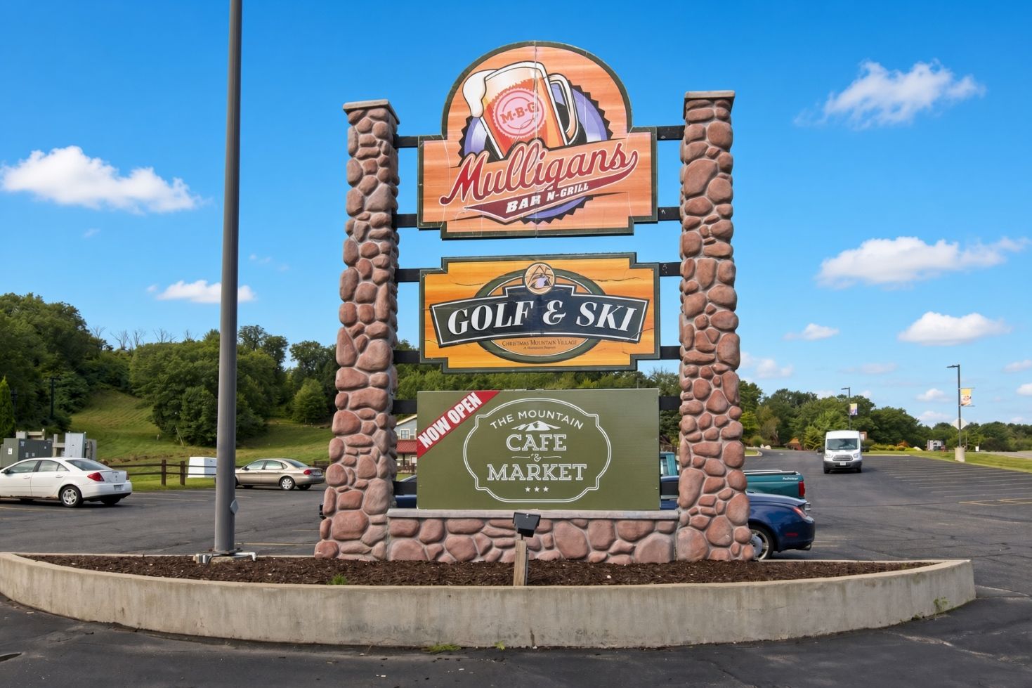 Une enseigne pour le bar-restaurant Mulligans N-Grill et le centre de golf et de ski, ainsi qu’une autre enseigne indiquant « Ouvert maintenant » pour le café-épicerie The Mountain Cafe Market.