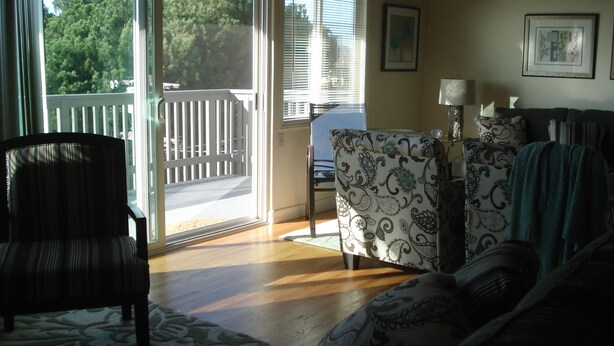 A living room with a wooden floor, a patterned armchair, a sofa, and a view of a deck through a glass door. - ***Romantic View Home Centrally Located in Windsor Hills, La Mesa*** (La Mesa)