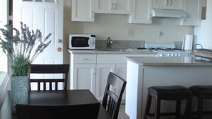 A kitchen with white cabinets, a microwave, a stove, and a dining area with a table and chairs. - ***Romantic View Home Centrally Located in Windsor Hills, La Mesa*** (La Mesa)