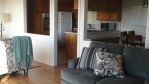 A living room with a grey sofa, patterned cushions, a wooden floor, and a kitchen in the background. - ***Romantic View Home Centrally Located in Windsor Hills, La Mesa*** (La Mesa)