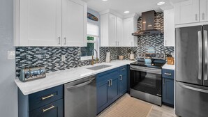 Una cocina moderna con armarios blancos, salpicadero blanco y negro, electrodomésticos de acero inoxidable y encimera azul.