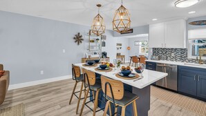 Una cocina moderna con una isla central, luces colgantes y un comedor con sillas.
