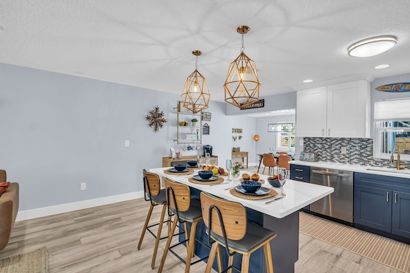 Una cocina moderna con una isla central, luces colgantes y un comedor con sillas.