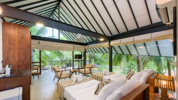 A hotel room with a large bed, a desk, and a chair. There is a TV on a stand and a window with a view of palm trees. - Thuduwa Camp (Rankethgama)