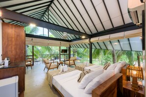 A hotel room with a large bed, a desk, and a chair. There is a TV on a stand and a window with a view of palm trees. - Thuduwa Camp (Rankethgama)