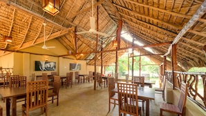 A spacious dining area with wooden tables and chairs, a high ceiling with a thatched roof, and large windows allowing natural light. - Thuduwa Camp (Rankethgama)