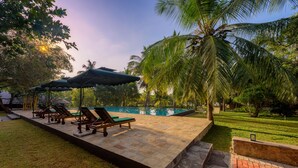 A swimming pool area with lounge chairs and umbrellas, surrounded by palm trees and a well-maintained lawn. - Thuduwa Camp (Rankethgama)