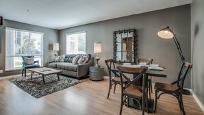 Un salon avec un canapé gris, une table basse, une table à manger avec des chaises, une lampe et un grand miroir.