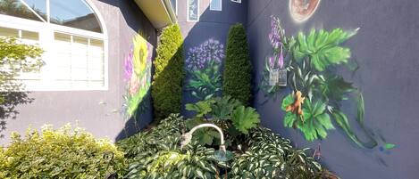 A courtyard with a garden, a mural, and a small birdcage.