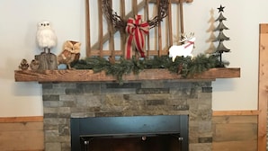 Un camino in pietra con mensola decorata da un'ghirlanda, un piccolo albero di Natale e una statuetta di renna.