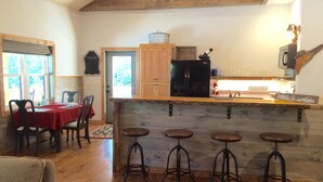 Cucina accogliente in stile baita, con isola in legno, sgabelli da bar e zona pranzo con tovaglia rossa.