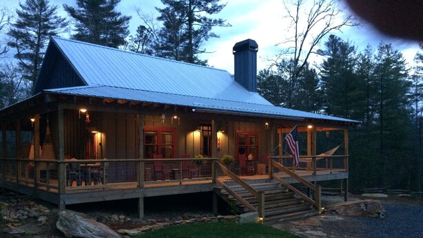 Una baita di legno con tetto in metallo, un portico con posti a sedere all'aperto e una bandiera americana.