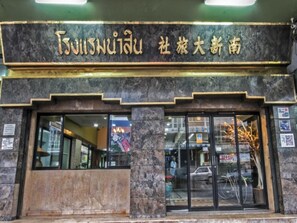 A building facade with a sign in a foreign script, large glass windows, and a stone base. - Numsin Hotel (Ratchaburi)
